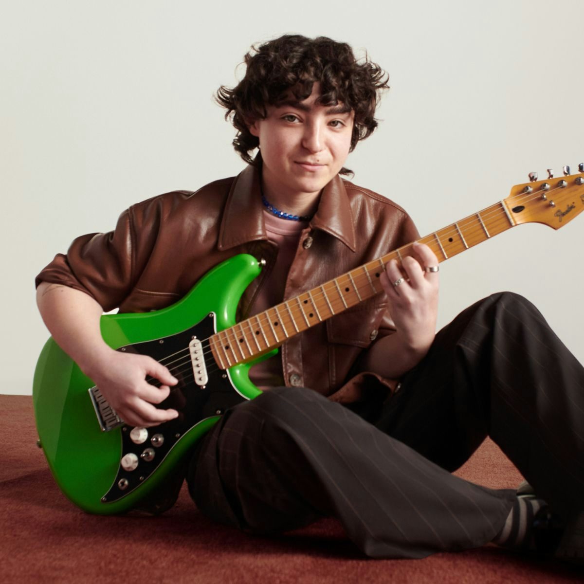 A portrait of Claud, looking at the camera with a smile, holding a green guitar